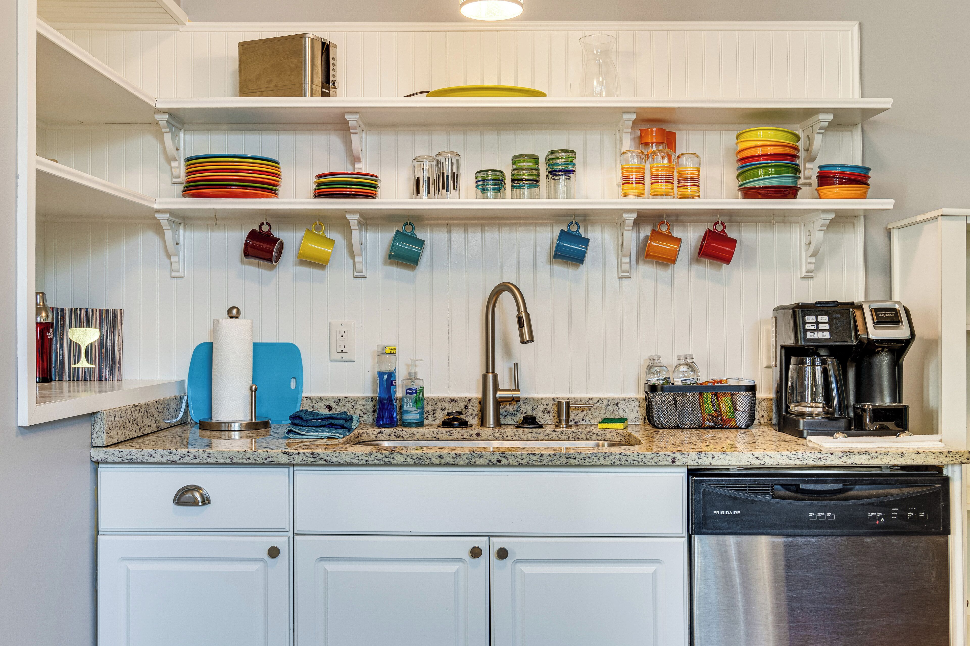 A kitchen with white cabinetry, a stainless steel dishwasher, and a countertop with various kitchen items.
