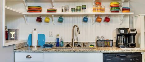 A kitchen with white cabinetry, a stainless steel dishwasher, and a countertop with various kitchen items.