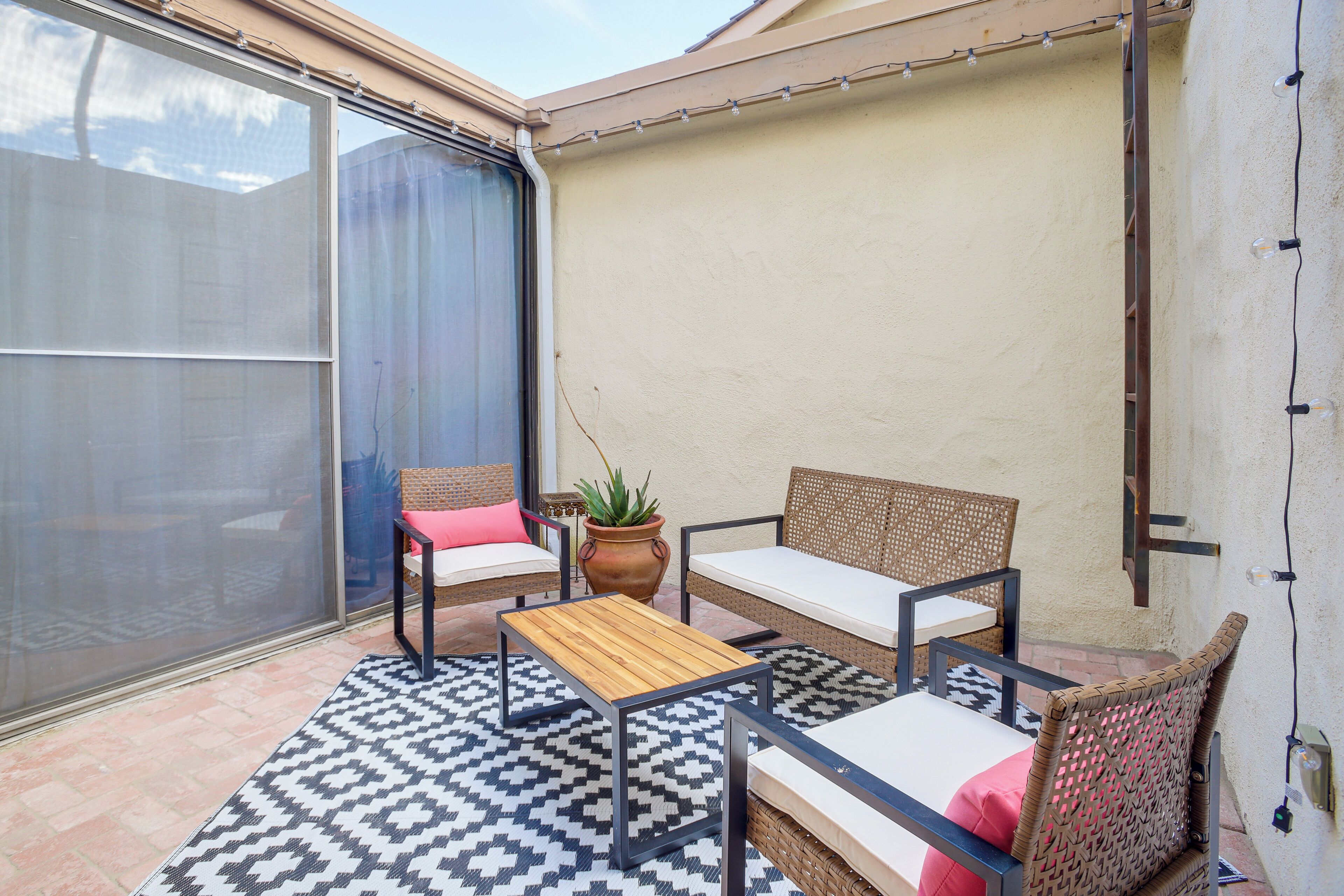 A patio with wicker furniture, a wooden table, and a potted plant.