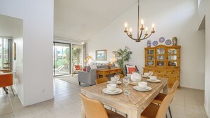 A spacious dining area with a wooden table set for four, surrounded by chairs. A chandelier hangs from the ceiling, and a wooden cabinet with glass doors is visible in the background. - Palm Desert Condo w/ Patio & Golf Course Views (Palm Desert)