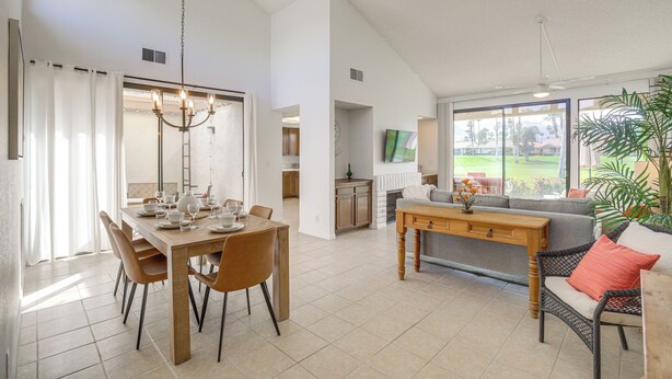 A spacious living area with a dining table, chairs, a sofa, and a large window offering a view of the outdoors. - Palm Desert Condo w/ Patio & Golf Course Views (Palm Desert)