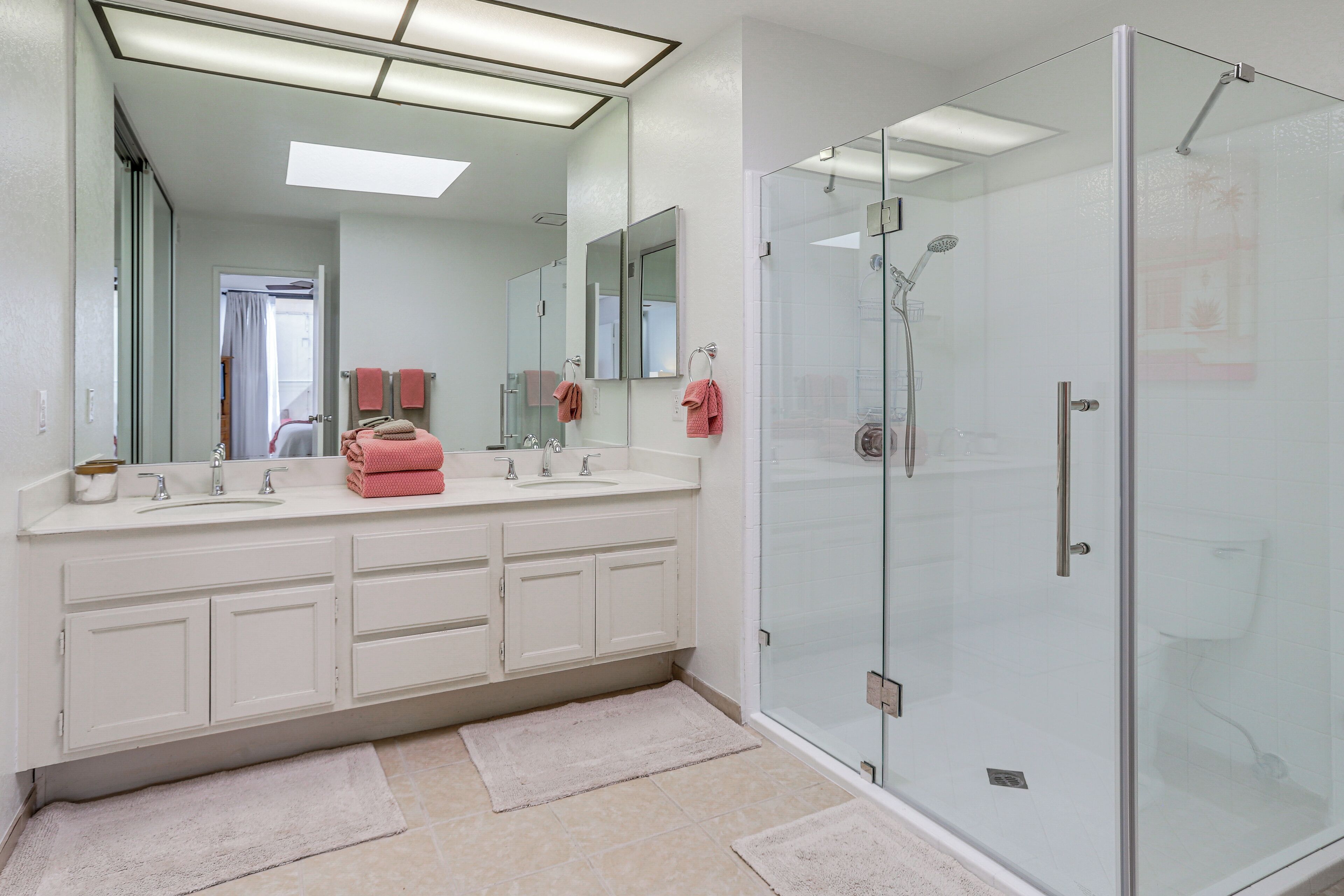A modern bathroom with a glass-enclosed shower, a large mirror, and a double sink vanity.