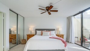 A bedroom with a large bed, two bedside tables with lamps, a ceiling fan, and a view through a sliding glass door. - Palm Desert Condo w/ Patio & Golf Course Views (Palm Desert)