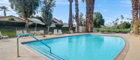 A swimming pool with a blue tiled edge, surrounded by palm trees and a fence.