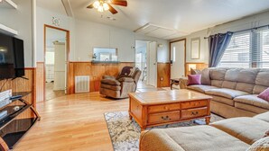 Ein geräumiges Wohnzimmer mit Holzboden, Deckenventilator, Fernseher, Sofa, Couchtisch und Kamin.