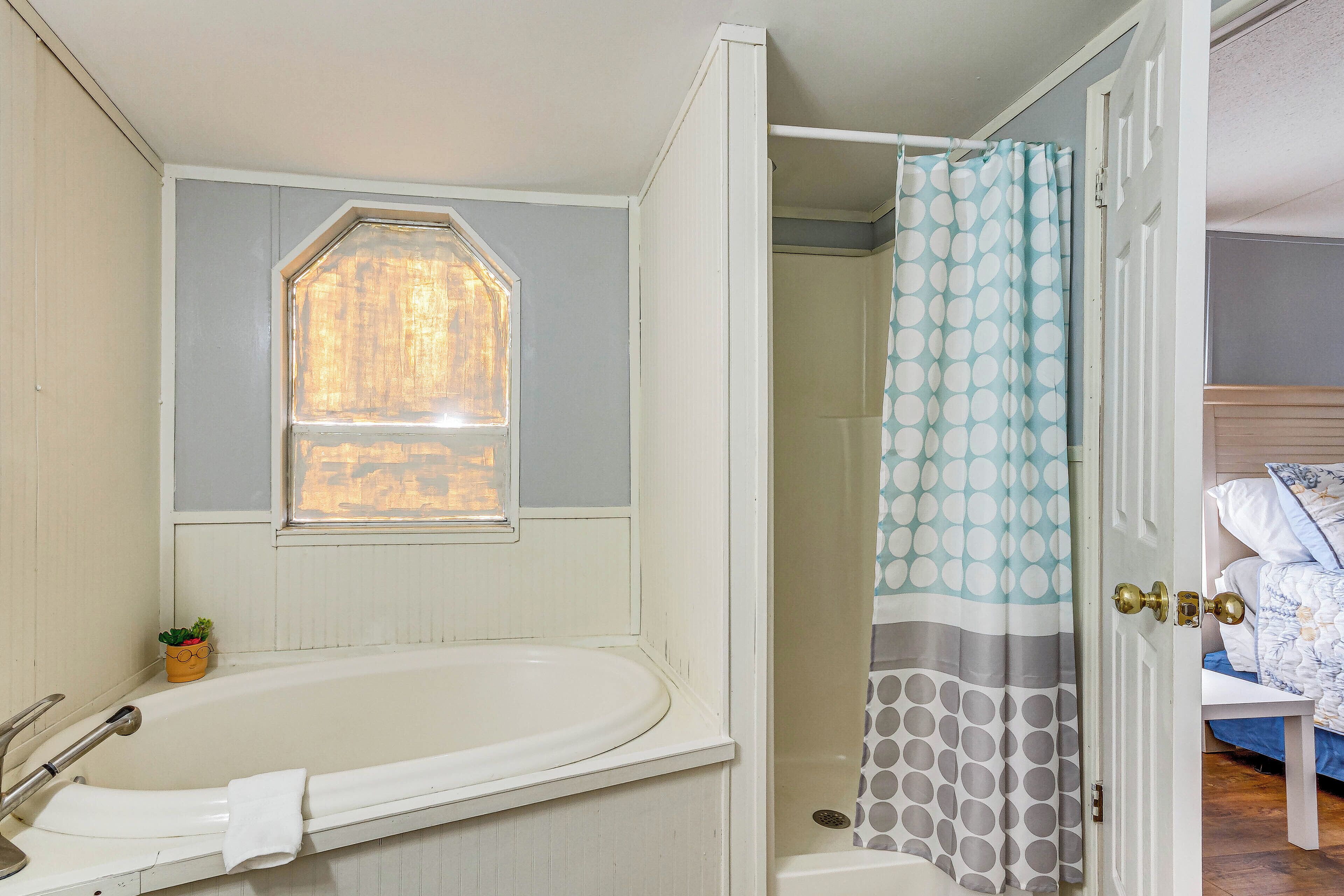 Un baño con bañera, ventana, cortina de ducha y puerta que da a un dormitorio.