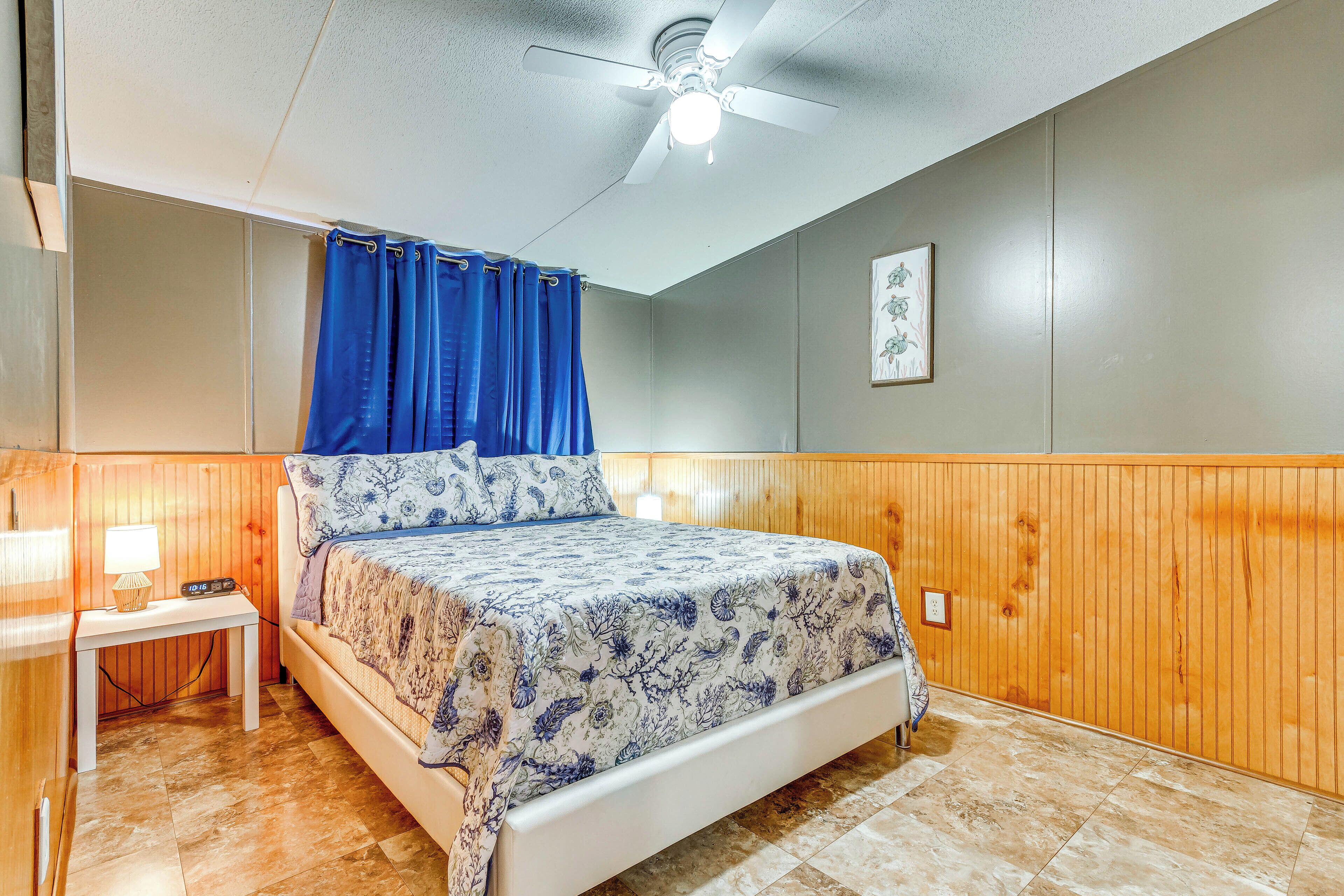 Une chambre à coucher avec un lit, une table de chevet, un ventilateur de plafond et des lambris en bois sur les murs.