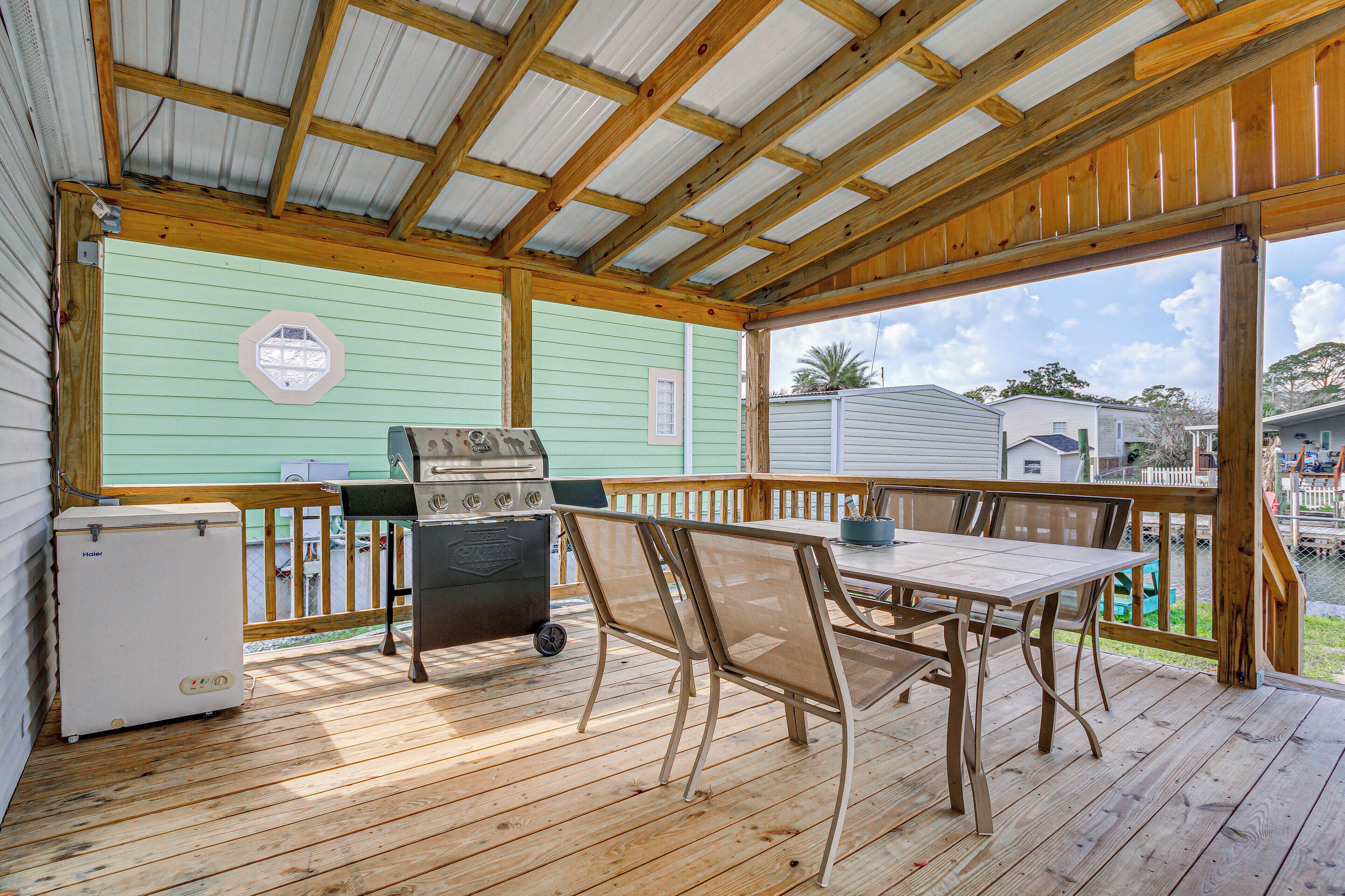 A covered outdoor deck with a table and chairs, a grill, and a refrigerator.