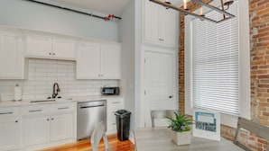 A modern kitchen with white cabinets, a microwave, and a sink. There is a dining table with chairs and a potted plant. - Downtown Hot Springs Condo Near Bathhouse Row! (Hot Springs)