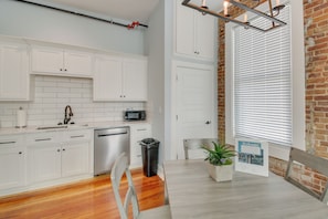 A modern kitchen with white cabinets, a microwave, and a sink. There is a dining table with chairs and a potted plant. - Downtown Hot Springs Condo Near Bathhouse Row! (Hot Springs)