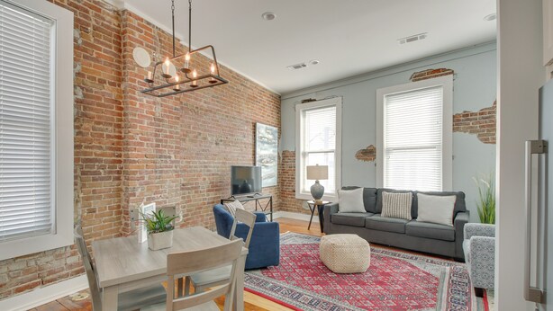 A living room with a brick wall, a dining table with chairs, a sofa, and a patterned rug. - Downtown Hot Springs Condo Near Bathhouse Row! (Hot Springs)