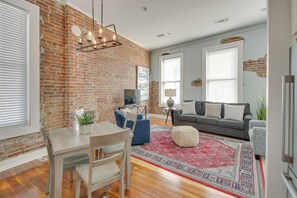 A living room with a brick wall, a dining table with chairs, a sofa, and a patterned rug. - Downtown Hot Springs Condo Near Bathhouse Row! (Hot Springs)