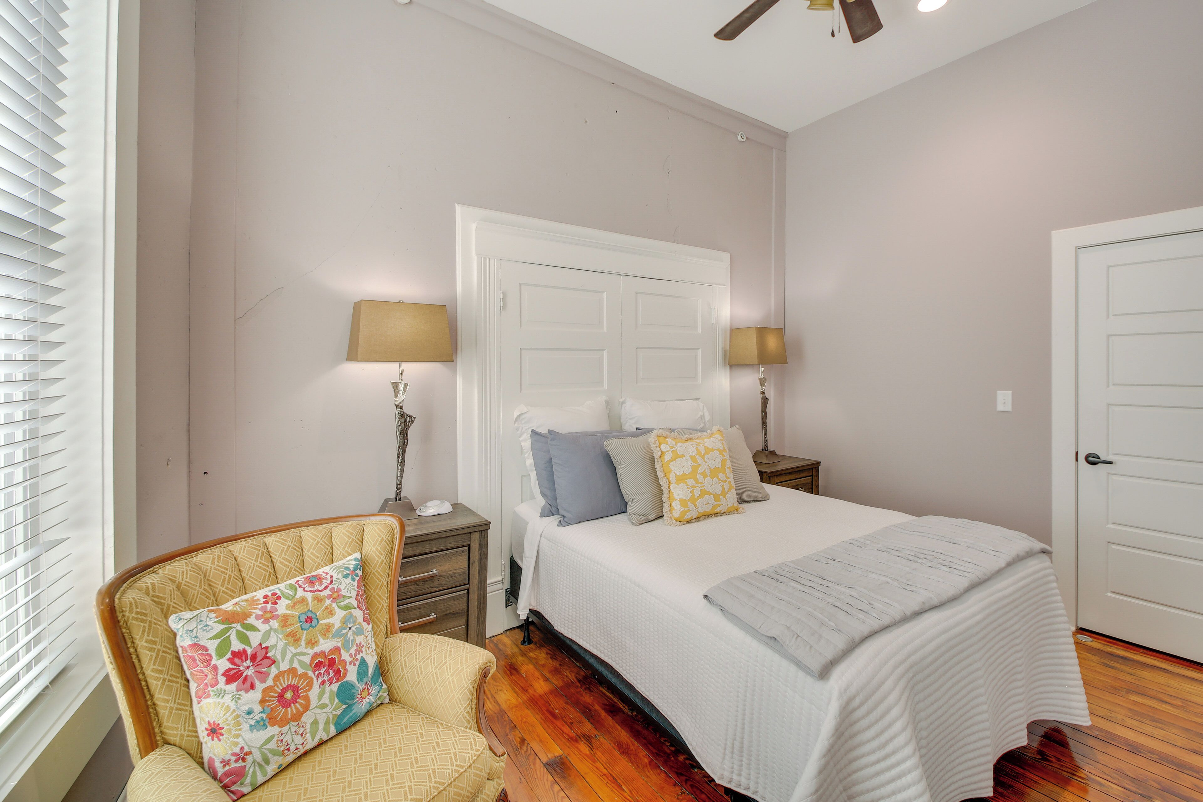 A bedroom with a bed, nightstands, a chair, and a door.