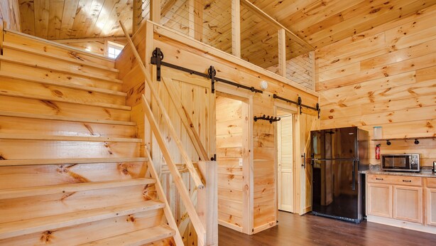 A wooden interior with a staircase, a sliding door, and a kitchen area with a refrigerator and microwave. - 'friends & Family' Rental Cabin w/ Hot Tub! (Somerset)