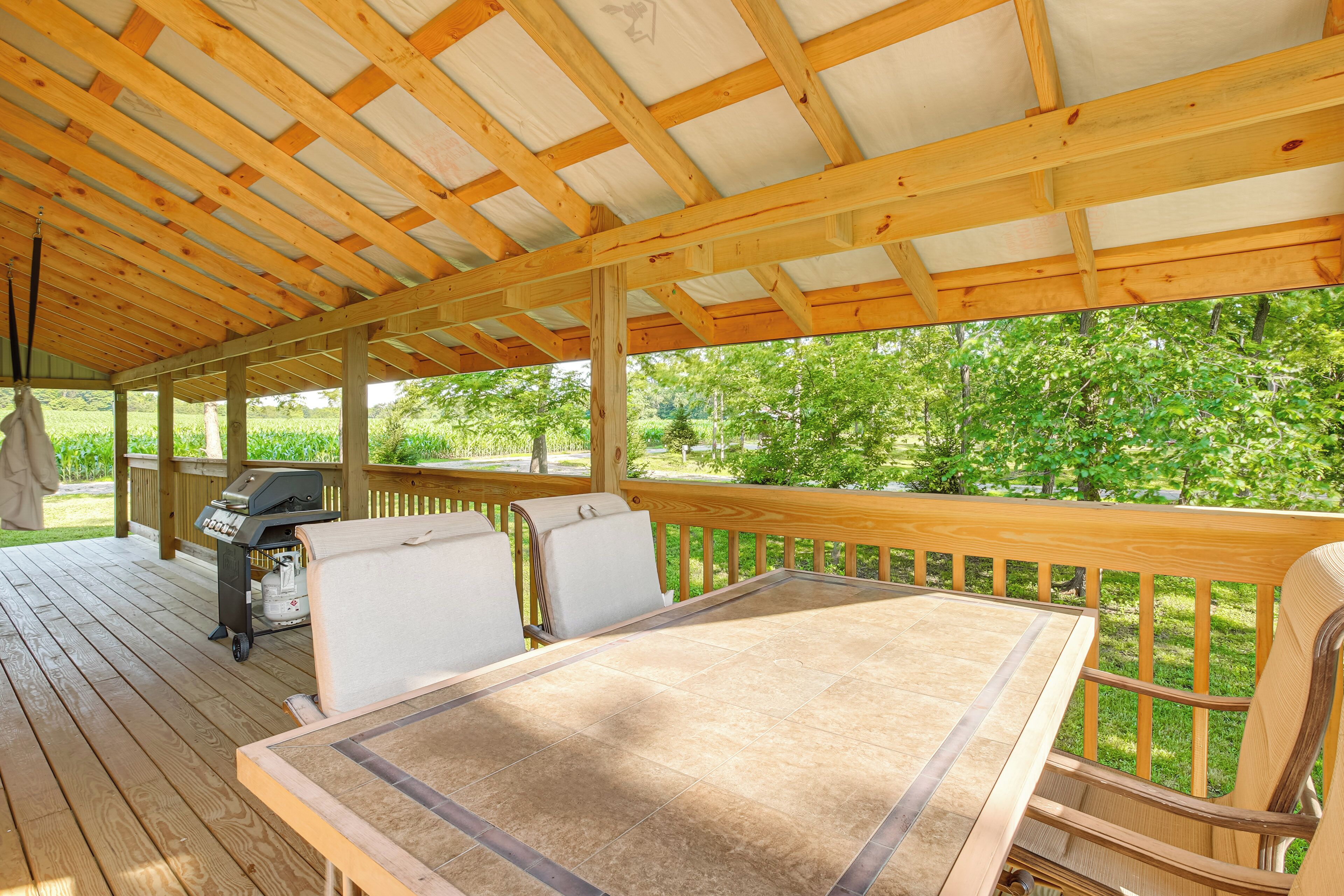 A covered outdoor deck with a grill, seating area, and a view of greenery.