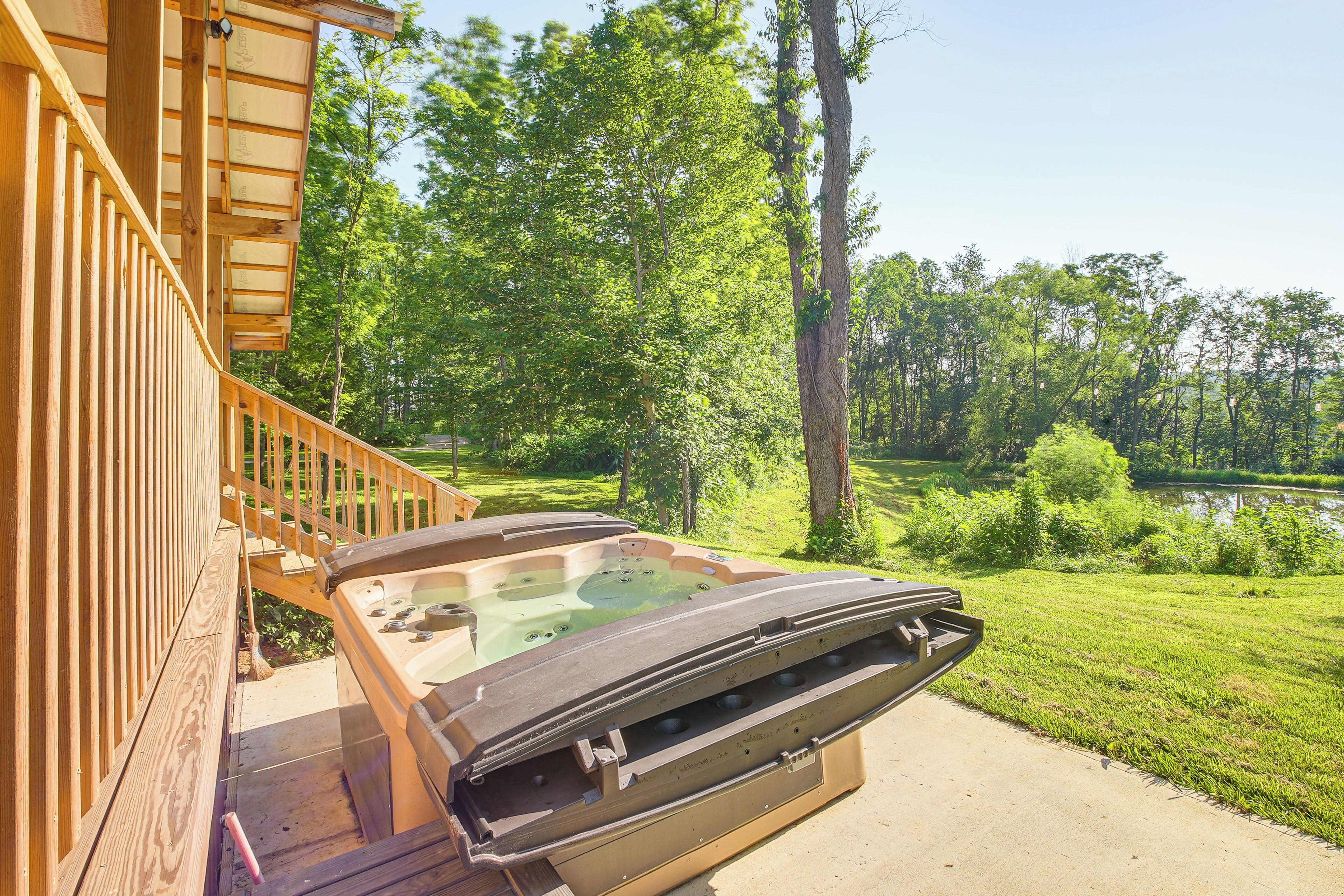 Een hottub met een houten terras en uitzicht op een vijver en bomen.