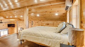 A wooden cabin bedroom with a bed, a lamp, and a mounted air conditioner. - 'friends & Family' Rental Cabin w/ Hot Tub! (Somerset)