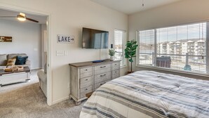 A bedroom with a bed, a dresser, a television, a ceiling fan, and a window with blinds. - Lake Ozark Condo w/ Water Views & Pool Access! (Lake Ozark)