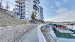 A waterfront residential building with multiple balconies, a concrete pathway, and a dock area with boats. - Lake Ozark Condo w/ Water Views & Pool Access! (Lake Ozark)