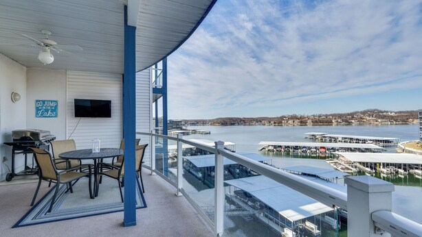 A covered outdoor area with a table and chairs, a grill, and a sign that reads "GO JUMP IN THE LAKE". - Lake Ozark Condo w/ Water Views & Pool Access! (Lake Ozark)