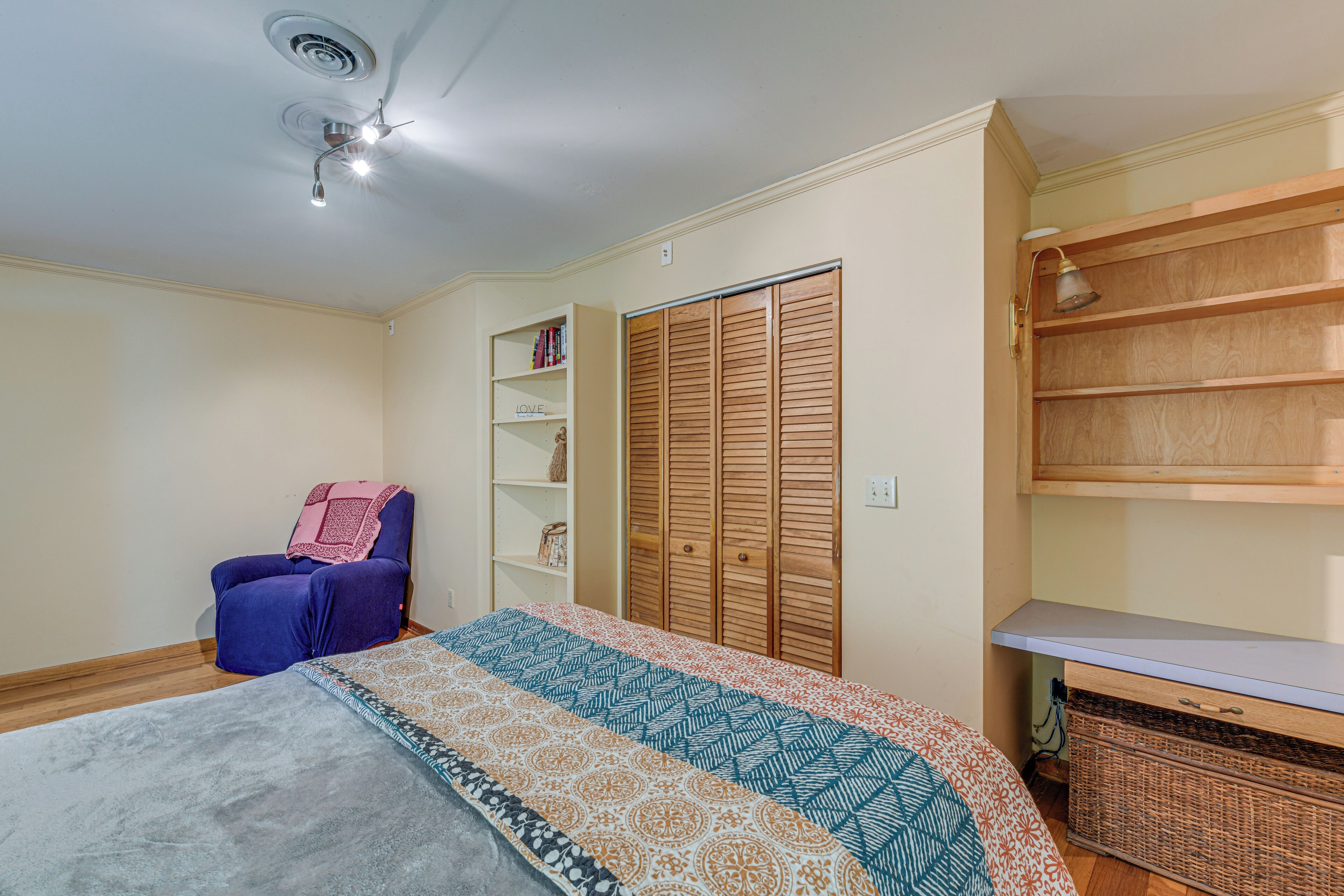 Ein Schlafzimmer mit Bett, Stuhl, Kleiderschrank und Schreibtisch mit Regalen.