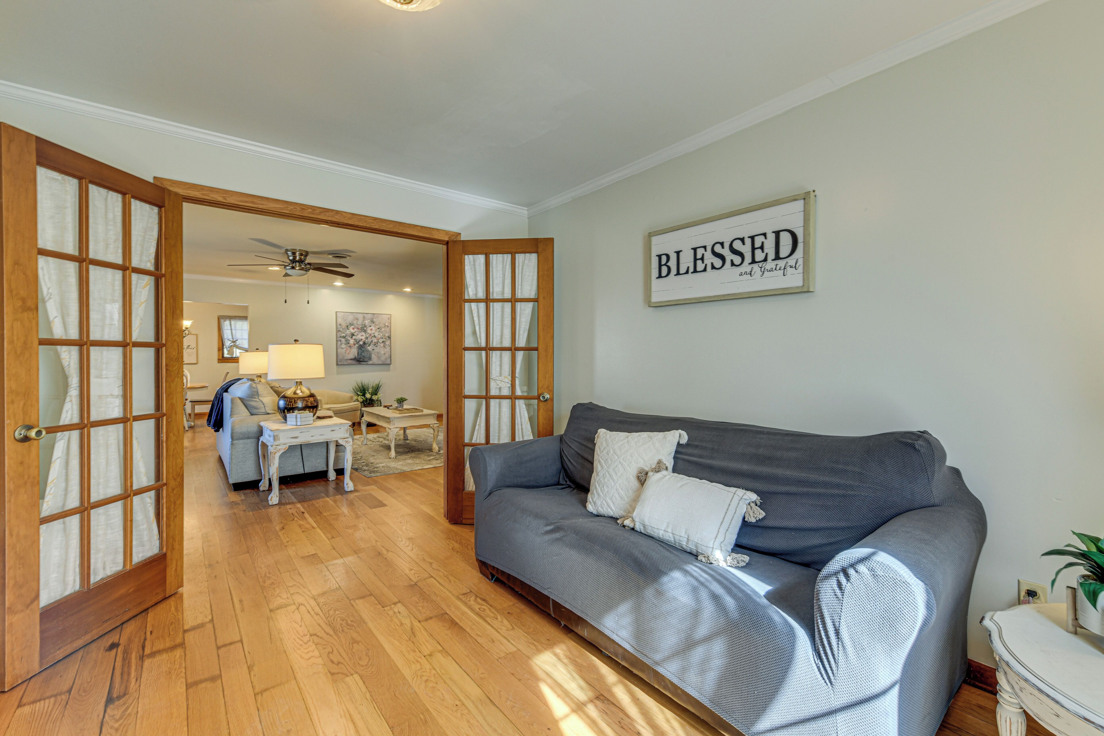 A living room with a grey sofa, wooden flooring, and a 'Blessed and Blessed' sign on the wall.