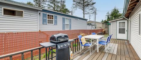A wooden deck with a grill, chairs, and a table.