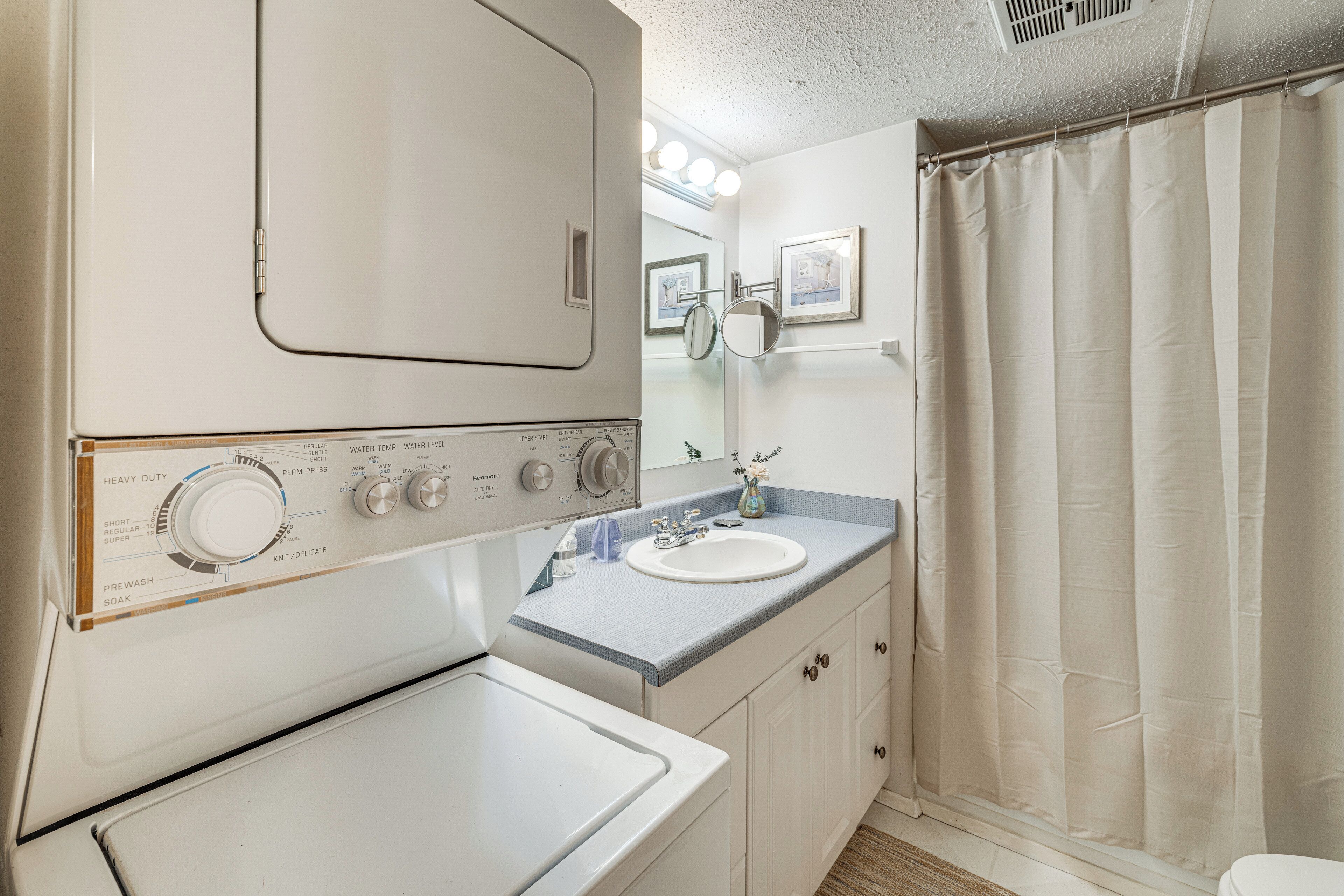 Baño pequeño con lavadora, lavamanos y cortina de ducha.