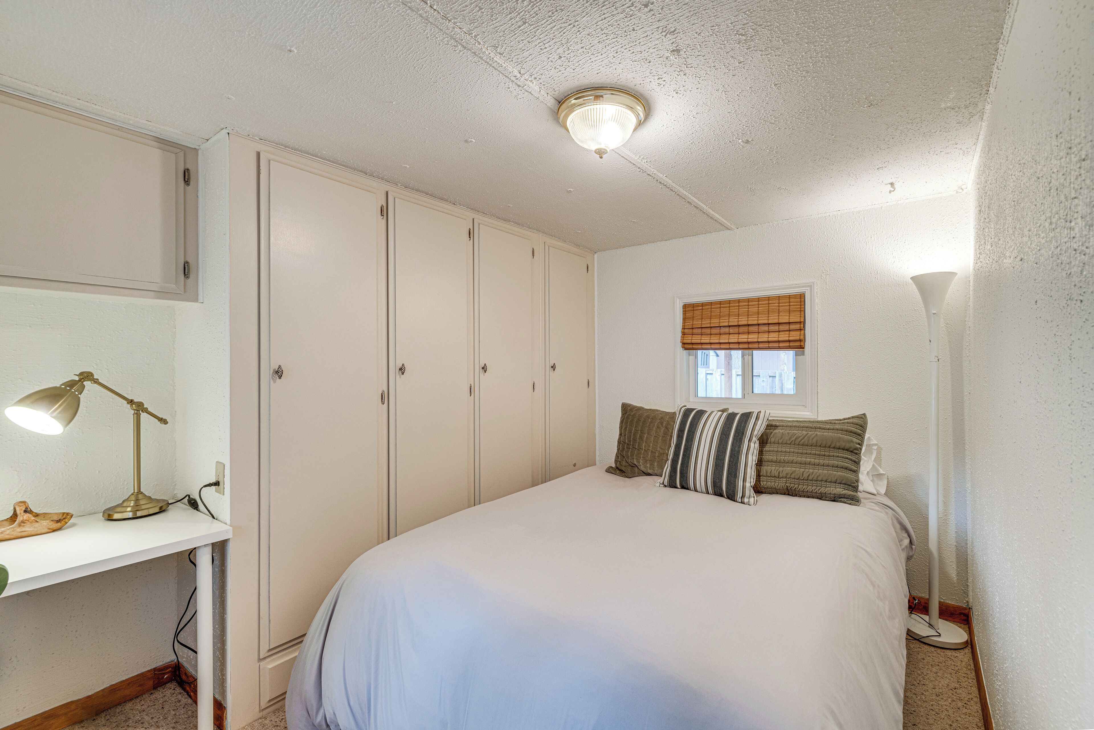 A bedroom with a bed, a desk with a lamp, a wardrobe, and a window with blinds.