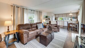 A living room with a brown leather sofa, a wooden coffee table, and a dining area with a table and chairs. - Rockaway Beach Home, Walk to Ocean, Pet Friendly! (Rockaway Beach)