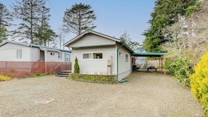 A single-story mobile home with a small porch and a covered outdoor area. - Rockaway Beach Home, Walk to Ocean, Pet Friendly! (Rockaway Beach)