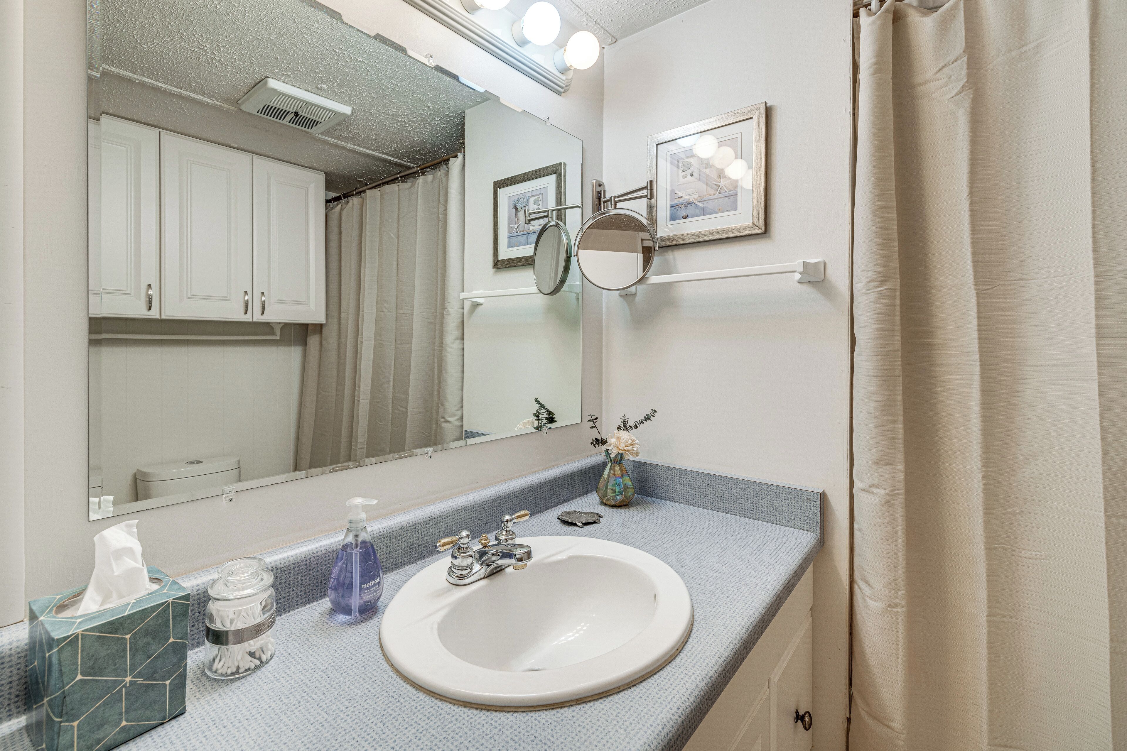 A bathroom with a white sink, a mirror, a towel dispenser, and a shower curtain.
