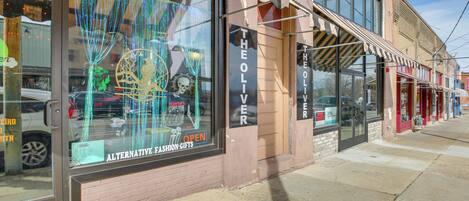 A storefront with a sign reading "THE OLIVER" and a window display featuring a mannequin and festive decorations.