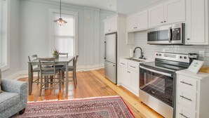 A modern kitchen with white cabinetry, stainless steel appliances, and a dining area with a patterned rug. - Modern Downtown Hot Springs Vacation Rental! (Hot Springs)