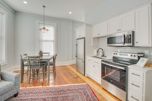 A modern kitchen with white cabinetry, stainless steel appliances, and a dining area with a patterned rug.