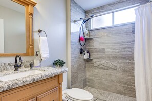 Ein Badezimmer mit Marmorwaschtisch, Holzausstattung, einer weißen Toilette, einer Duschkabine mit Glastür und einer Steinwand.