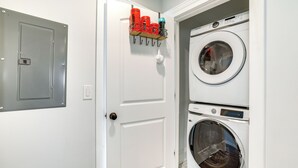 A laundry room with two stacked front-loading washing machines, a metal utility door, and a wall-mounted drying rack with red and blue containers. - Long Branch Getaway - Walk to Beaches & Dining! (Long Branch)