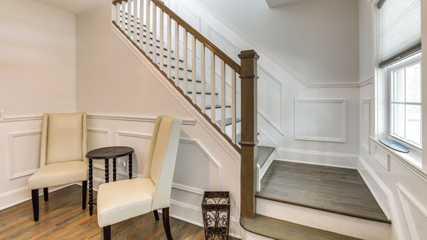A staircase with wooden railings and a white wall with paneling. There are two chairs and a small table in the room. - Long Branch Getaway - Walk to Beaches & Dining! (Long Branch)