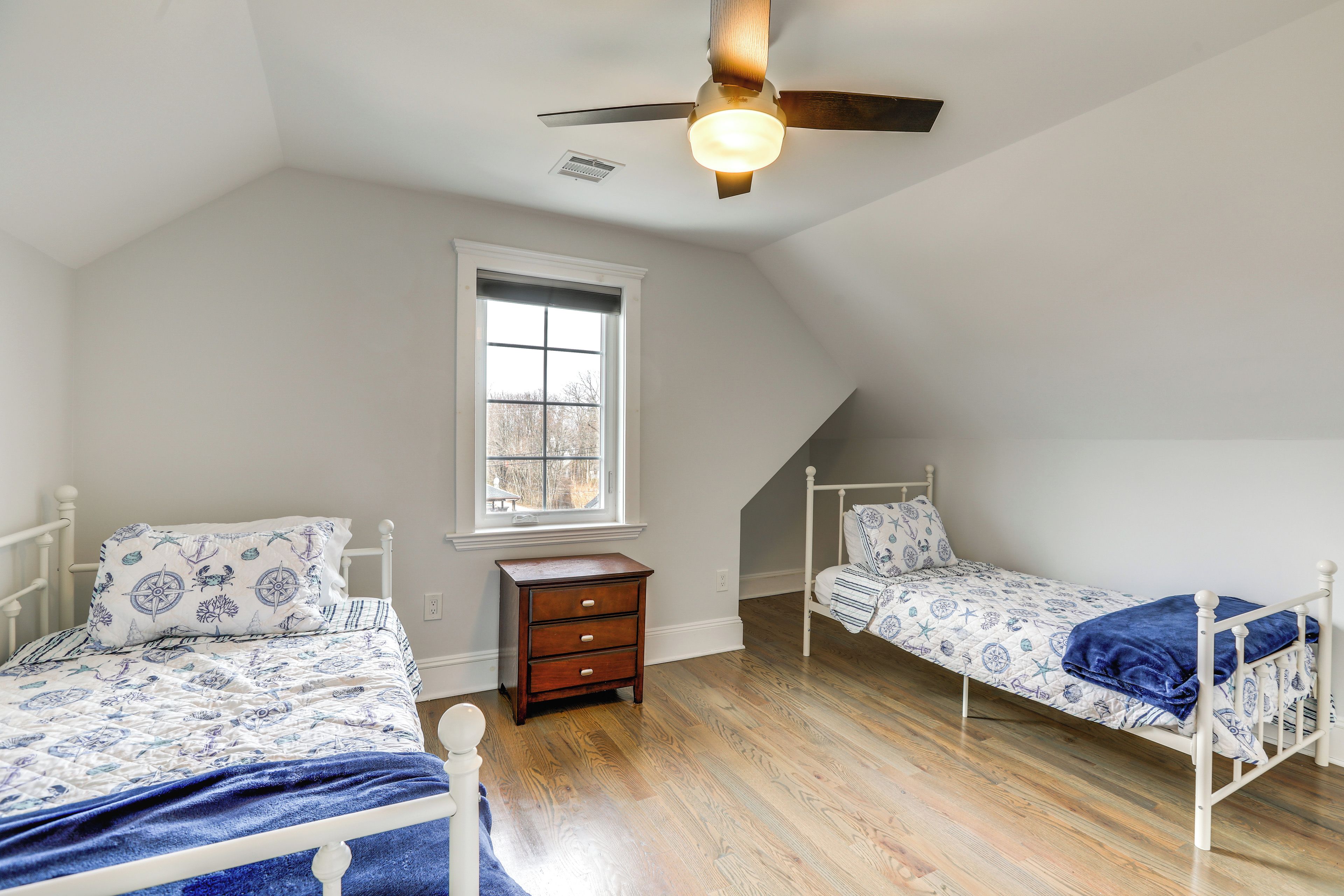 A bedroom with two single beds, a nightstand, a window, and a ceiling fan.