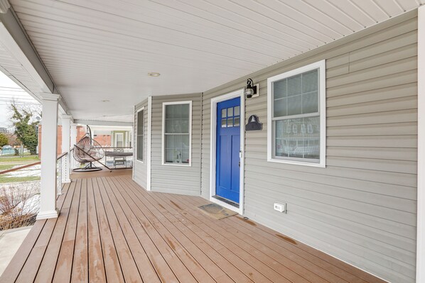 A covered porch with a blue door, white trim, and a hanging chair. - Long Branch Getaway - Walk to Beaches & Dining! (Long Branch)