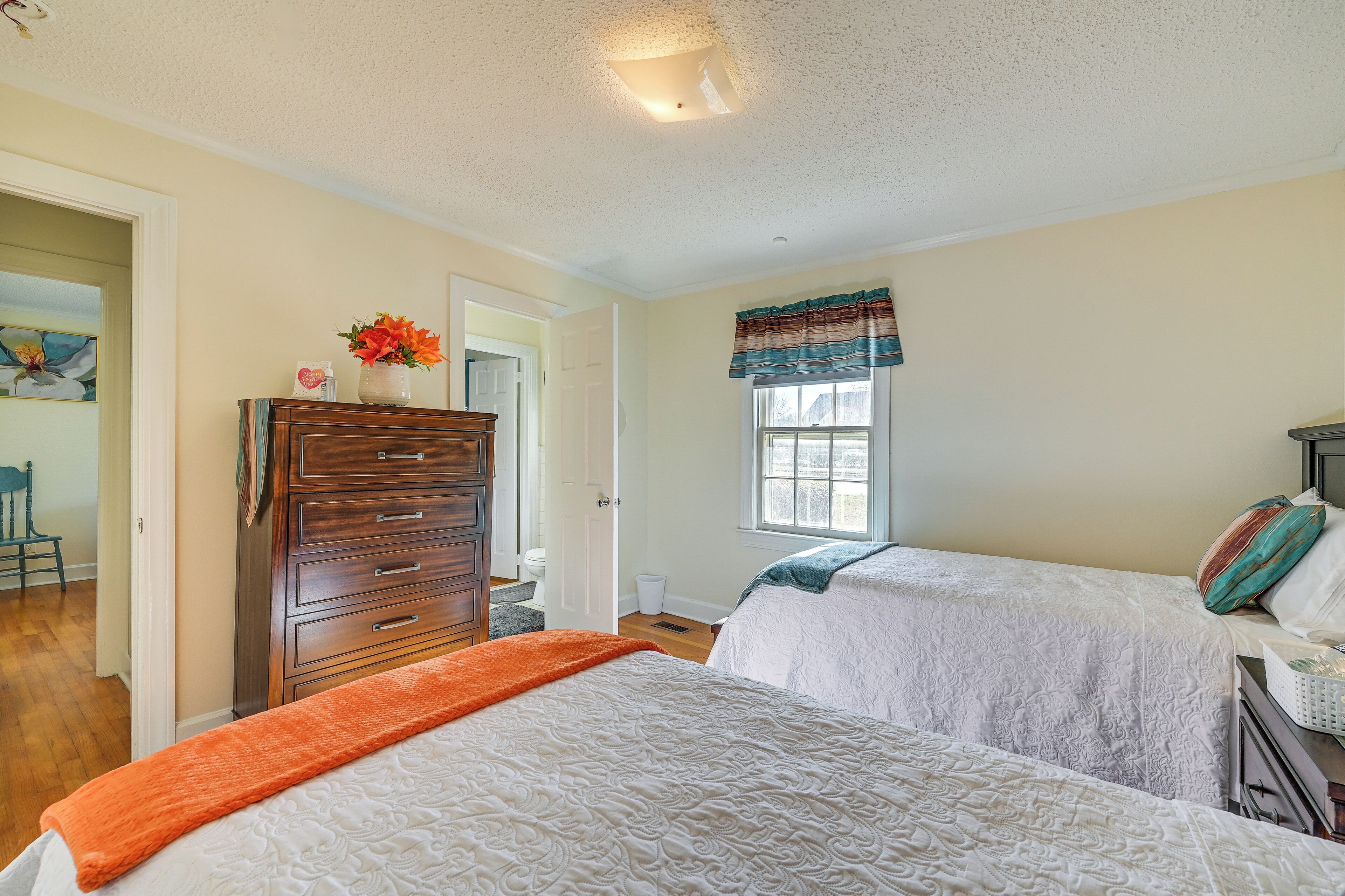 A bedroom with two beds, a dresser, and a window with curtains.