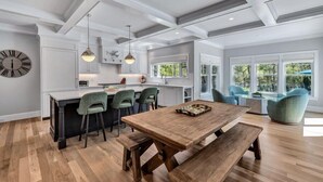 Une cuisine moderne dotée d’un îlot central, de tabourets de bar, de luminaires suspendus et d’une table à manger avec des bancs.