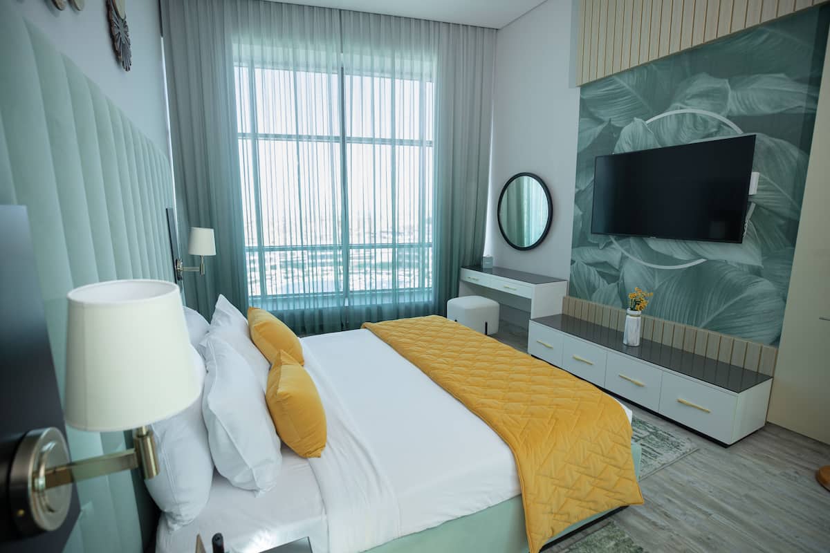 Une chambre d’hôtel avec un lit, une table de chevet avec une lampe, un téléviseur fixé au mur et une fenêtre avec des rideaux.