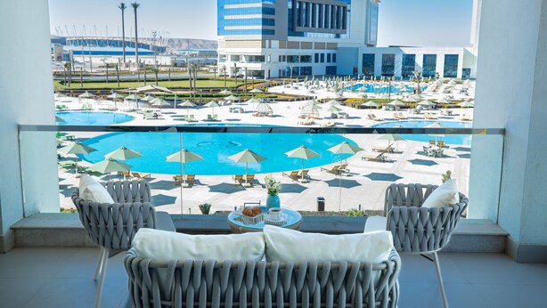 A balcony with wicker chairs, a table with a vase and a bowl, and a view of a pool area with umbrellas and lounge chairs. - Tolip Hotel Olympic International City (New Cairo)