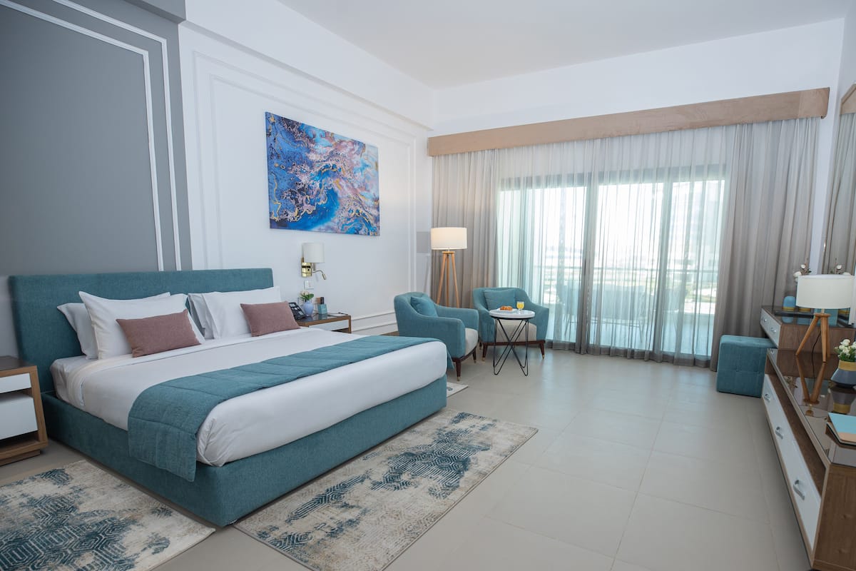 Une chambre d’hôtel moderne dotée d’un grand lit, d’un bureau, de deux chaises et offrant une vue sur la ville grâce à de grandes fenêtres.