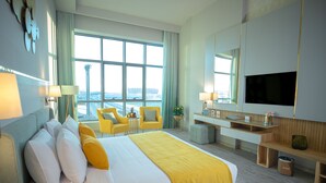 A hotel room with a large bed, a desk, a TV, and a view of the city. - Tolip Hotel Olympic International City (New Cairo)