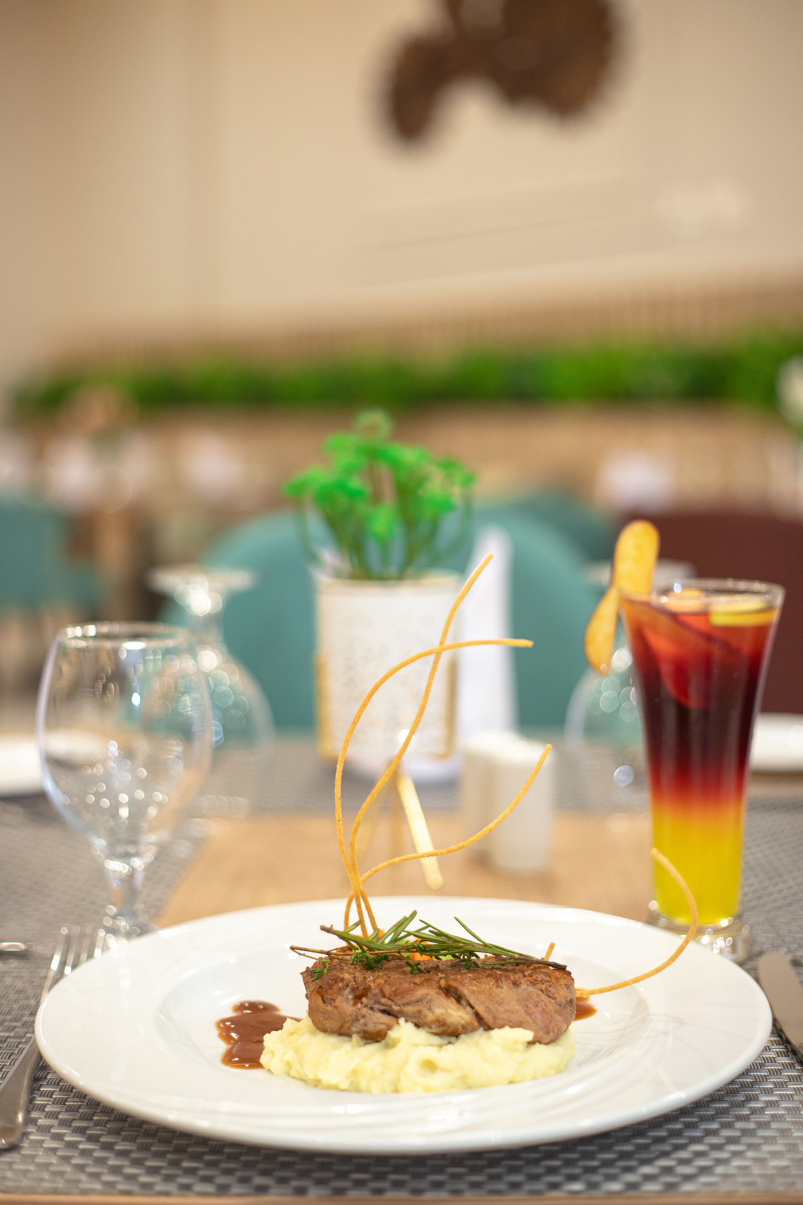 A dining table with a plate of food, a glass of drink, and a vase with a plant.