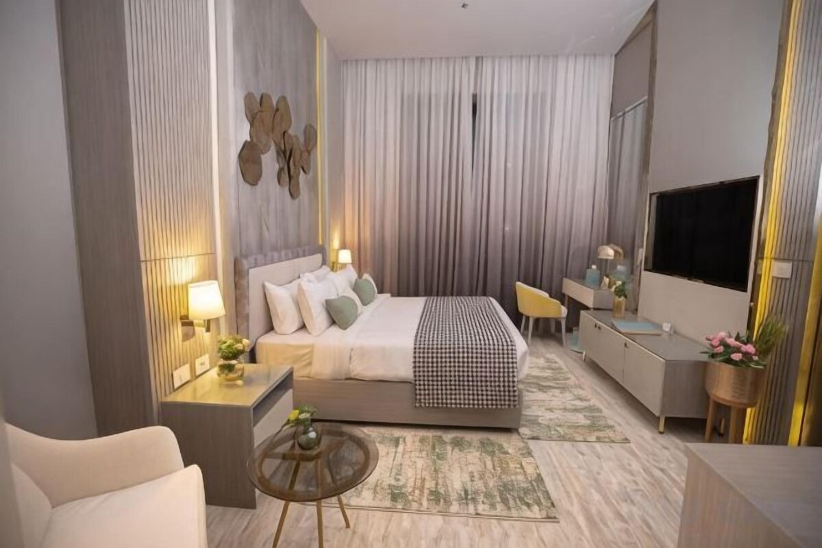 Habitación de hotel moderna con una cama grande, mesitas de noche, un escritorio, una silla, un televisor y una pequeña mesa redonda.