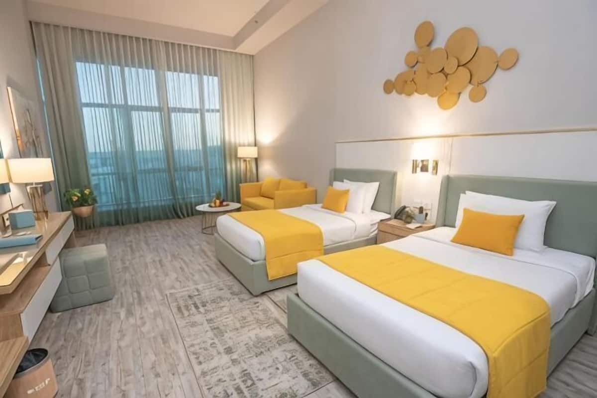 Une chambre d’hôtel avec deux lits, un bureau, une chaise, une petite table et une fenêtre avec des rideaux.