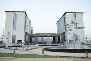 A modern building with a central entrance and a circular water feature. - Tolip Hotel Olympic International City (New Cairo)